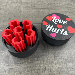 Een set van zes rode shibari rope spikes in een doosje met de tekst "Love Hurts"
