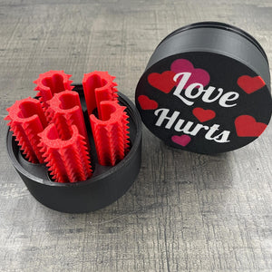 Een set van zes rode shibari rope spikes in een doosje met de tekst "Love Hurts"