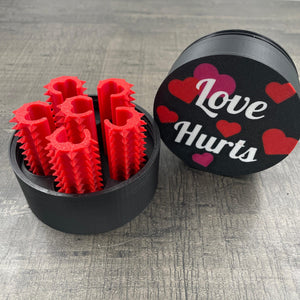 Een set van zes rode shibari rope spikes in een doosje met de tekst "Love Hurts"