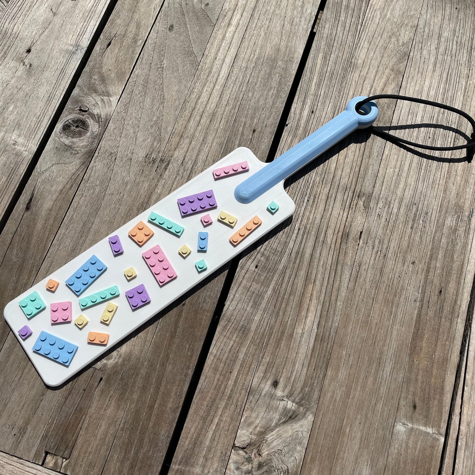 Een BDSM paddle in wit met pastel-kleurige bouwsteentjes en een blauw handvat