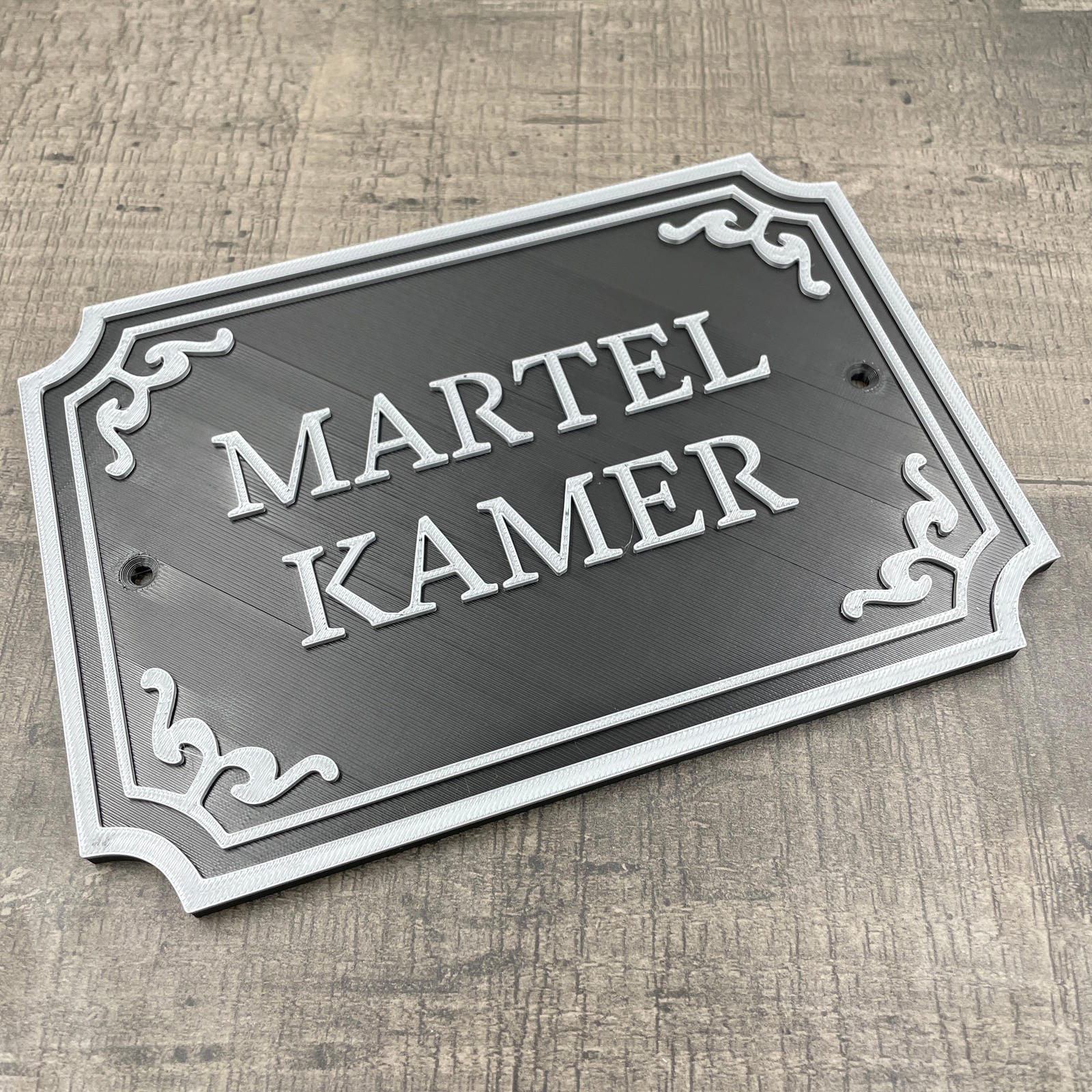 Een zwart deurbordje met de tekst "Martelkamer" in silveren letters.