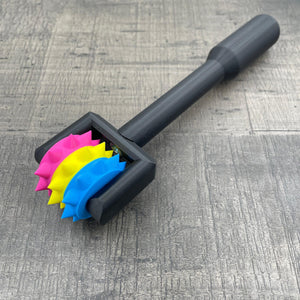 Een BDSM pinwheel met een zwart handvat en wieltje in de kleuren van non-binaire vlag