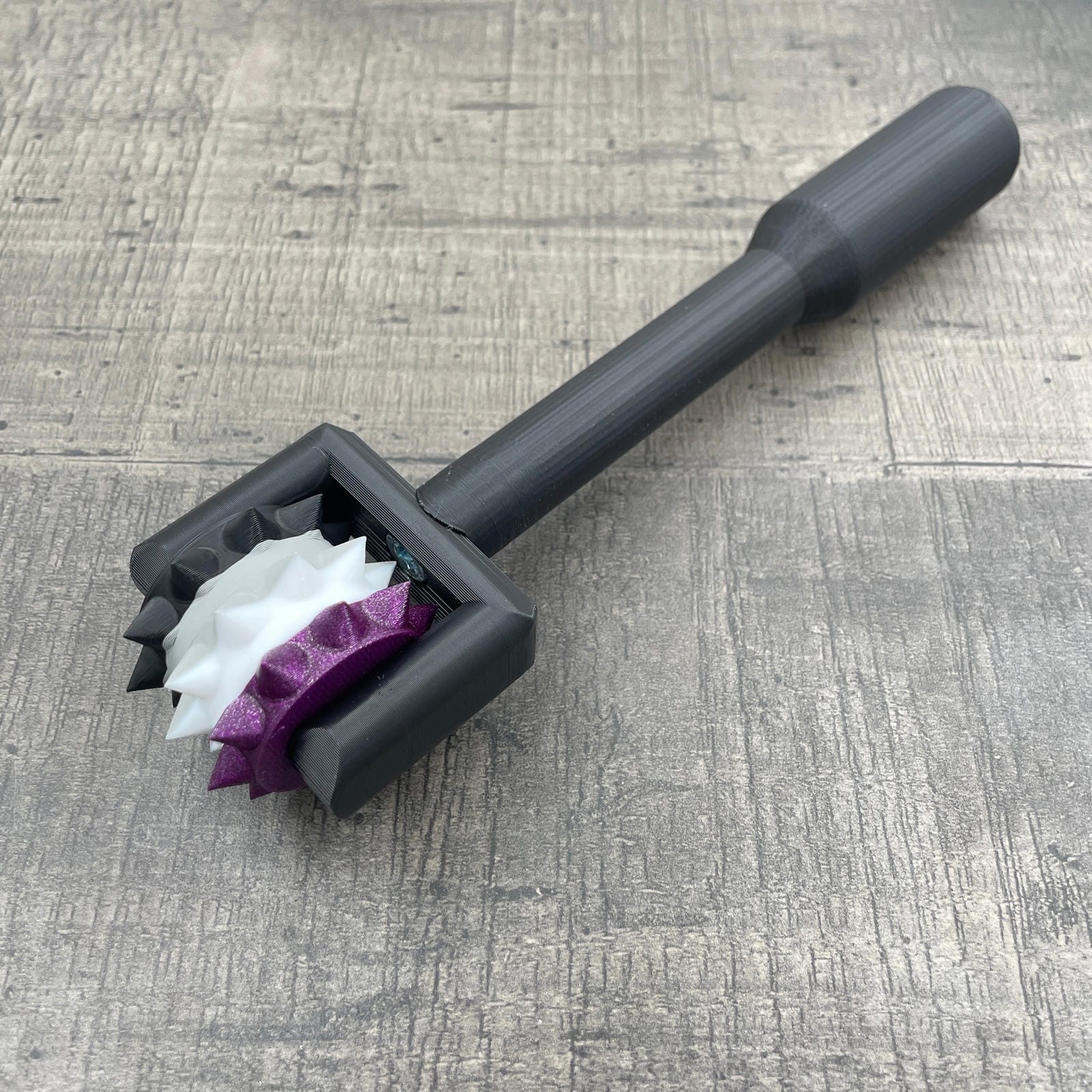 Een BDSM pinwheel met een zwart handvat en wieltje in de kleuren van a-seksuele vlag